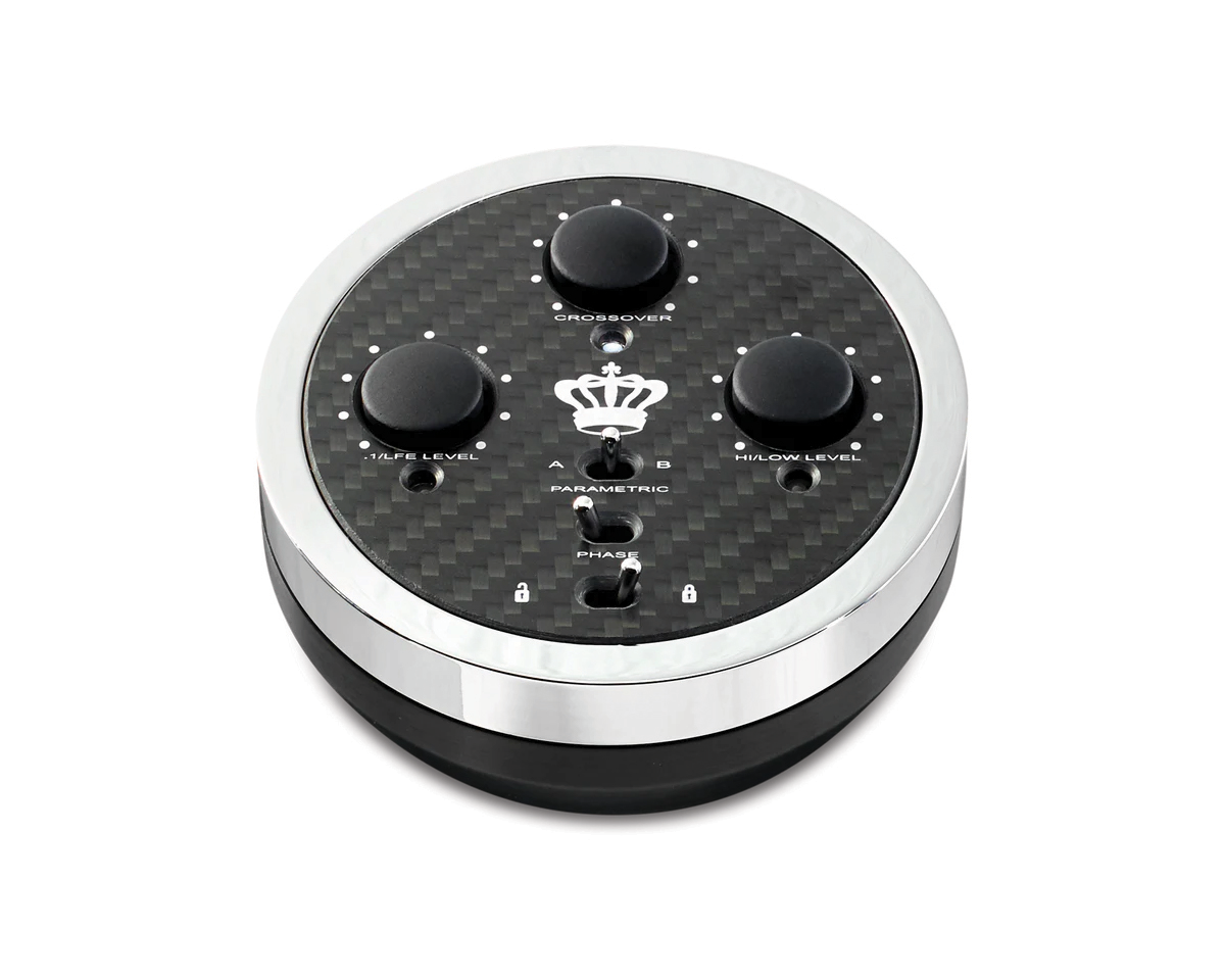 A round, black and silver audio control device with three knobs labeled "Crossover," "+1/LFE Level," and "Hi/Low Level." A crown symbol is centered.