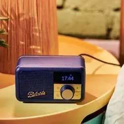 A vintage-style blue radio sits on a yellow table, displaying the time "17:44." Warm lighting and a cozy, rustic background create a nostalgic ambiance.