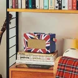 Bookshelf with books above, a guitar to the left, and a radio with a British flag design on a table, expressing a cozy, music-themed vibe.