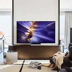 Modern living room with a large TV displaying vibrant abstract art. Neutral tones in decor, plush sofa with a blanket, and floor-to-ceiling windows.