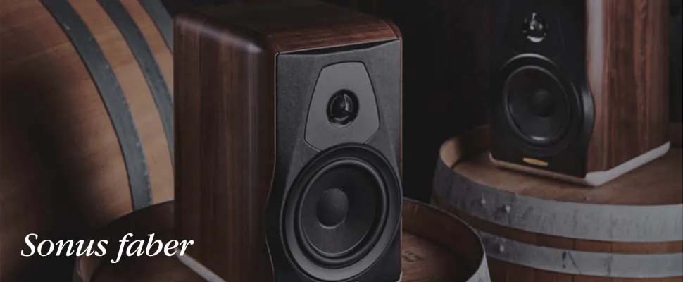 Two elegant Sonus faber speakers with wooden enclosures are placed on wine barrels, conveying a luxurious and vintage aesthetic.