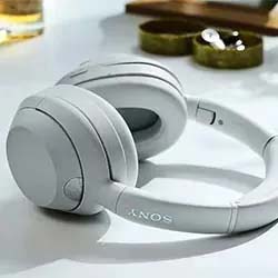 White over-ear headphones on a light-colored surface, with subtle shadows. Nearby are small decorative items, creating a modern and relaxed atmosphere.