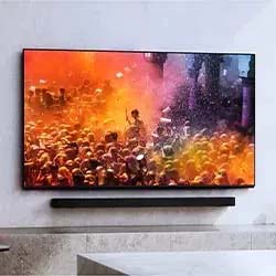 Flat-screen TV displaying a vibrant festival with a crowd covered in colorful powder. The energetic scene conveys joy and celebration. Wall-mounted setup.