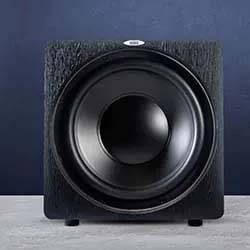 A sleek black subwoofer with a prominent circular speaker in the center, set against a dark blue wall and placed on a light gray surface.