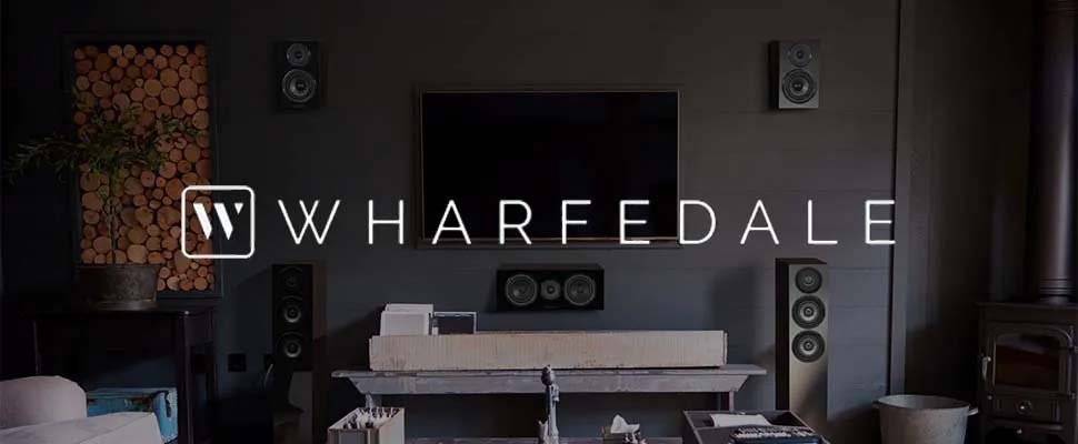 Modern living room with large TV, surround sound speakers, and fireplace. Sophisticated, cozy ambiance. Text overlaid: "Wharfedale" with logo.