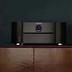 Black audio receiver with a circular display, flanked by two speakers, sits on a wooden cabinet against a dark wall, conveying a sleek, modern ambiance.