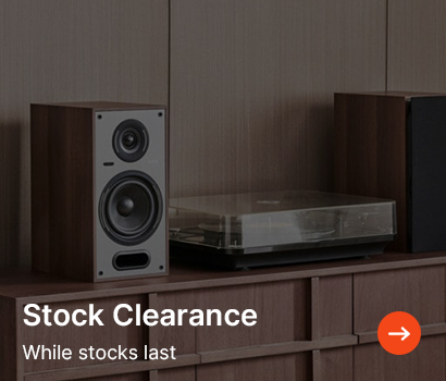 Wooden speaker and turntable on a cabinet in a dimly lit room. Text reads ‘Stock Clearance. While stocks last’ with an orange arrow icon.