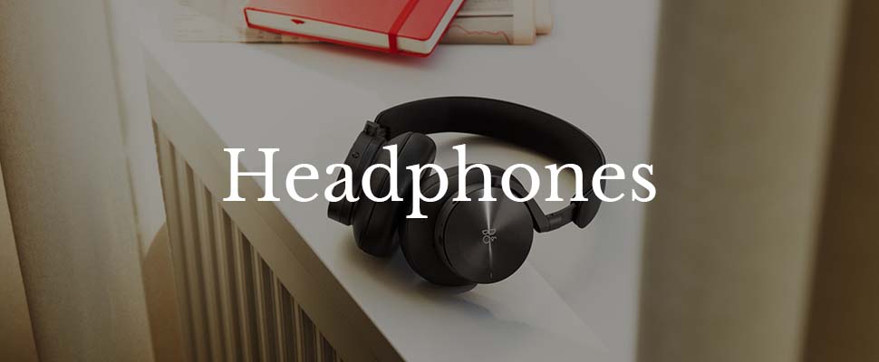 A pair of black headphones rests on a white surface beside red books, partially illuminated by soft natural light. The word "Headphones" overlays the image.