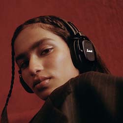 A person with long hair and braids wears headphones, gazing confidently at the camera. The background is a warm red, conveying a bold and stylish vibe.