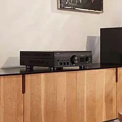 Audio receiver on a wooden cabinet against a light wall. Minimalist decor with a black object and framed artwork adding modern style.