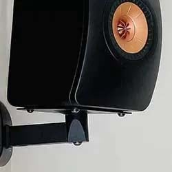 A sleek black speaker mounted on a wall with a copper-colored tweeter in the center. The design is modern, conveying a sense of sophistication.