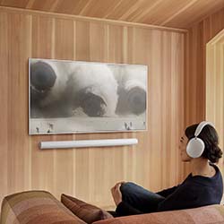 A person wearing headphones sits on a couch, watching a nature scene on a wall-mounted TV in a cozy, wood-paneled room. The atmosphere is calm and focused.