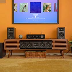 Stylish wood-finish entertainment center with a vintage speaker system and modern stereo on orange background. Mounted TV displays music interface. Cozy ambiance.