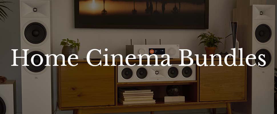 A modern home entertainment setup with a wooden cabinet, two tall white speakers, a central speaker system, and a decorative plant, conveying a cozy, stylish atmosphere. Text overlay reads "Home Cinema Bundles."