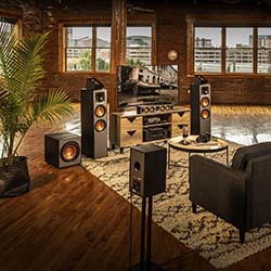Spacious loft with a modern home theater setup, featuring large speakers, a flat-screen TV, and a stylish rug. Large windows provide cityscape views.