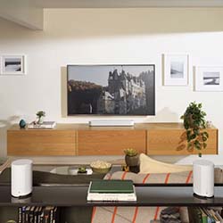 Modern living room with a large wall-mounted TV displaying a castle. Minimalist wood furniture, plants, and framed photos create a cozy, stylish ambiance.
