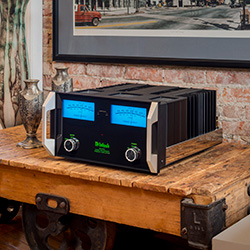 High-end audio amplifier with glowing blue dials sits on a rustic wooden table against a brick wall, evoking a vintage-modern aesthetic.