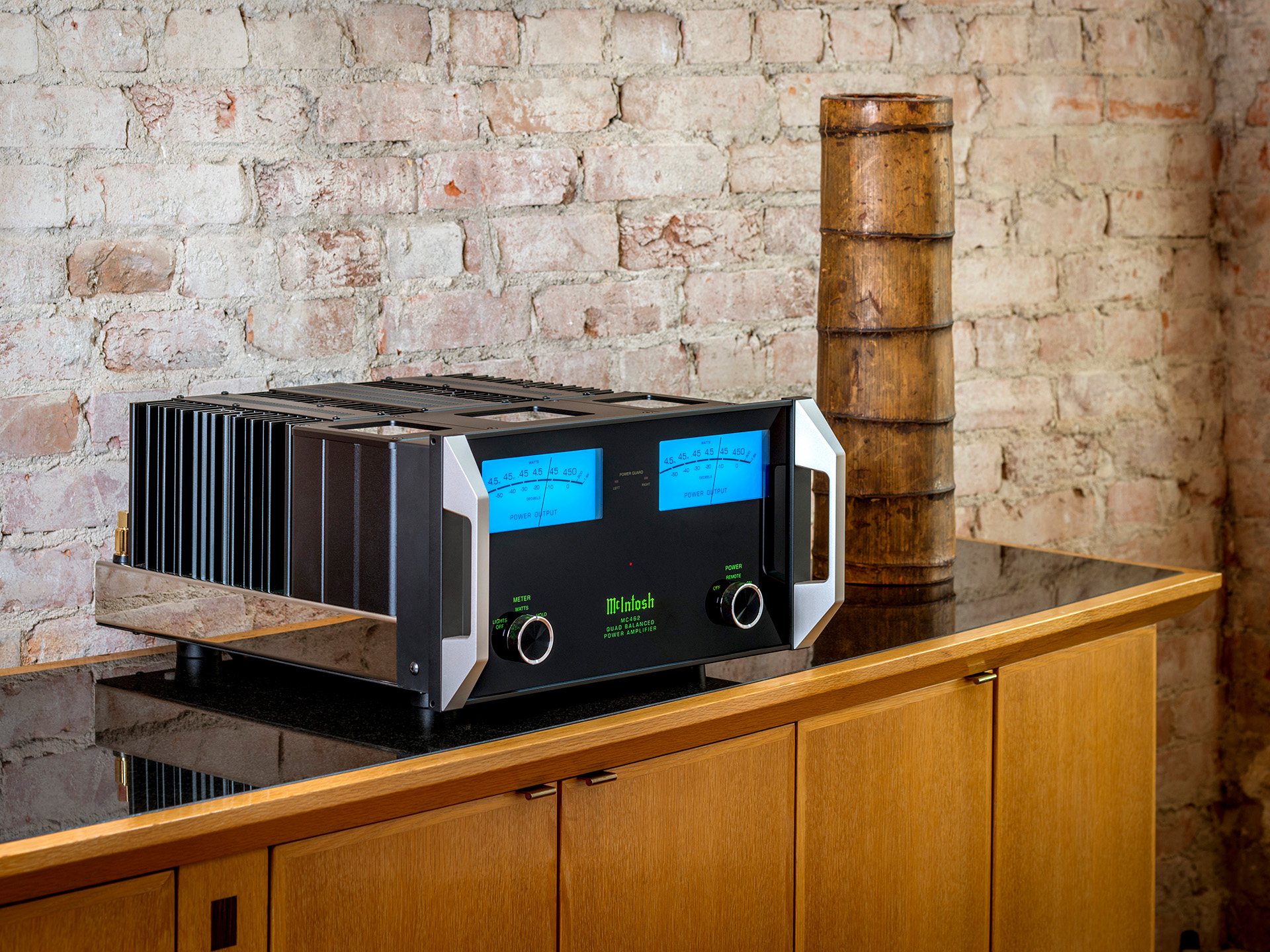 High-end audio amplifier with glowing blue meters and sleek black design on a modern wooden cabinet. Rustic brick wall backdrop, warm ambiance.