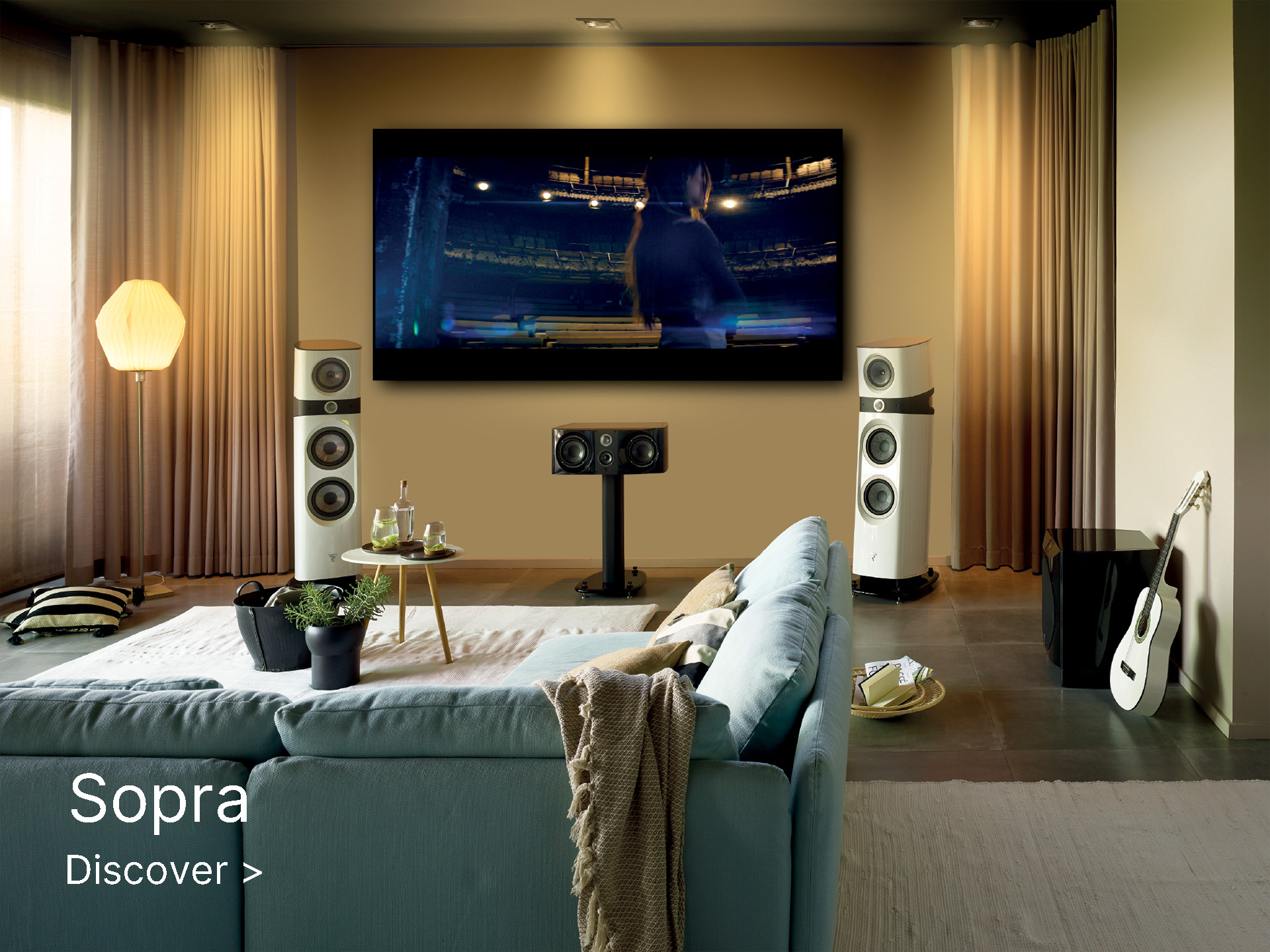Modern living room with a large flat-screen TV displaying a seated audience scene. Surrounded by speakers, a cozy sofa, guitar, and a warm ambiance.