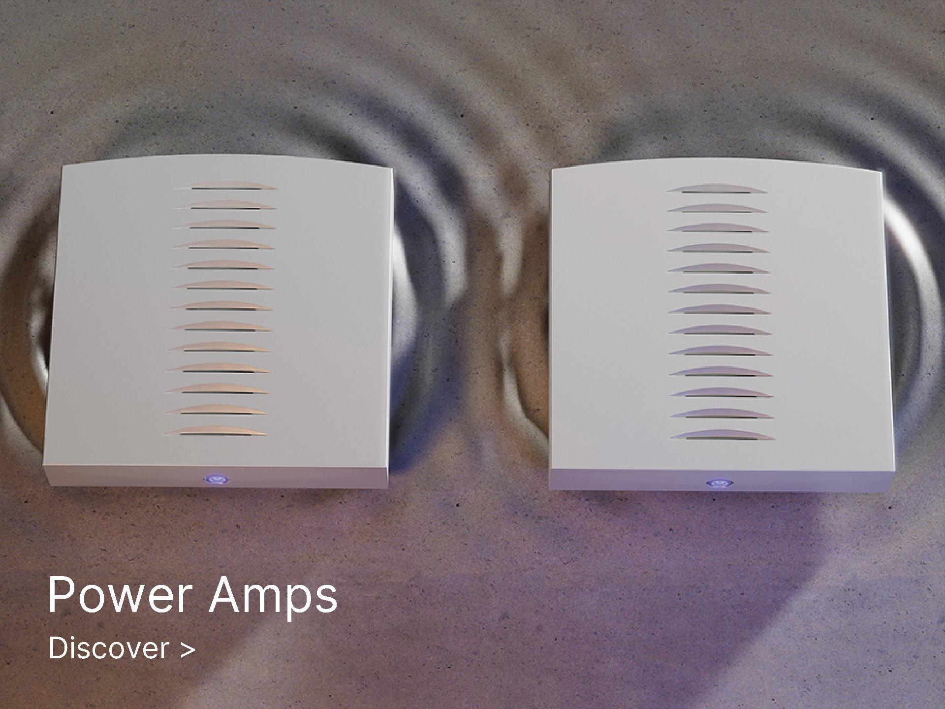 Two sleek white power amplifiers with vented tops are placed on a reflective surface, creating a rippled effect. Text reads "Power Amps" and "Discover."