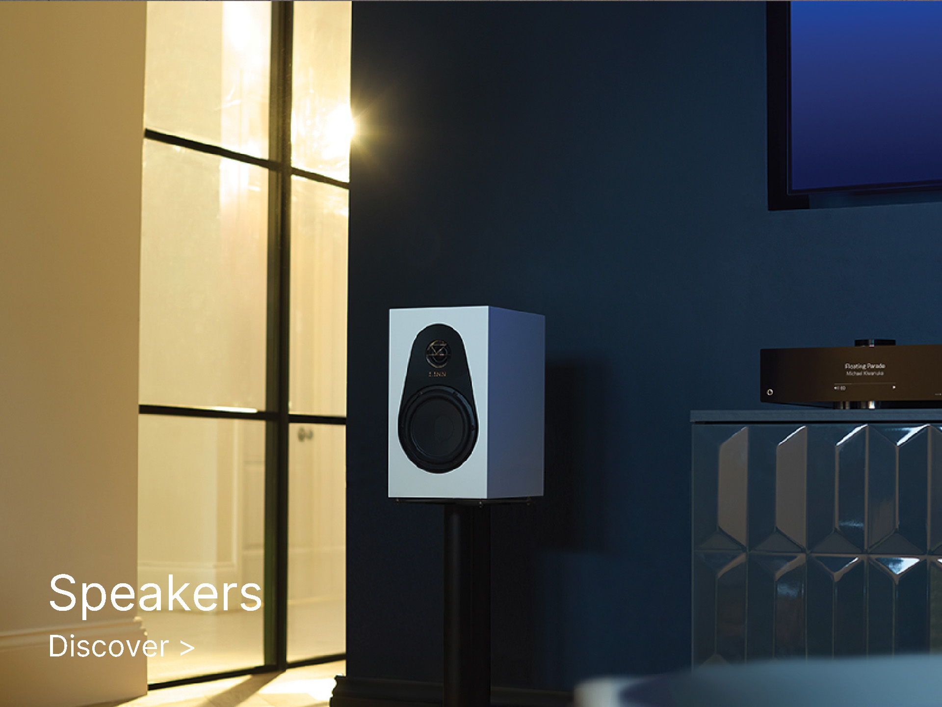 Modern white speaker in a dimly lit room with dark blue walls and minimalist decor. Text reads "Speakers Discover." Calm, sophisticated atmosphere.