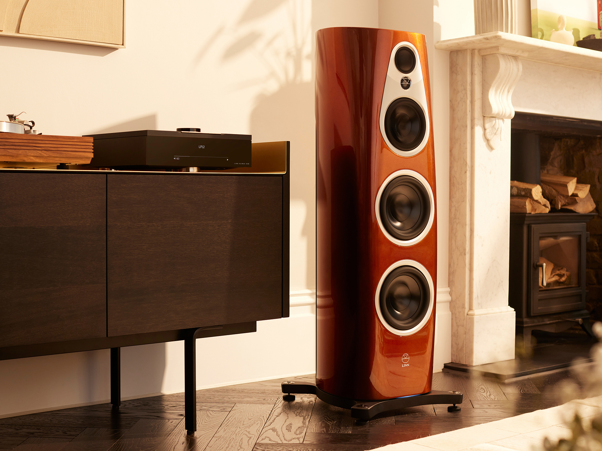 Elegant living room with a tall, glossy wooden speaker next to a dark, modern cabinet. Warm light casts soft shadows, creating a cozy atmosphere.