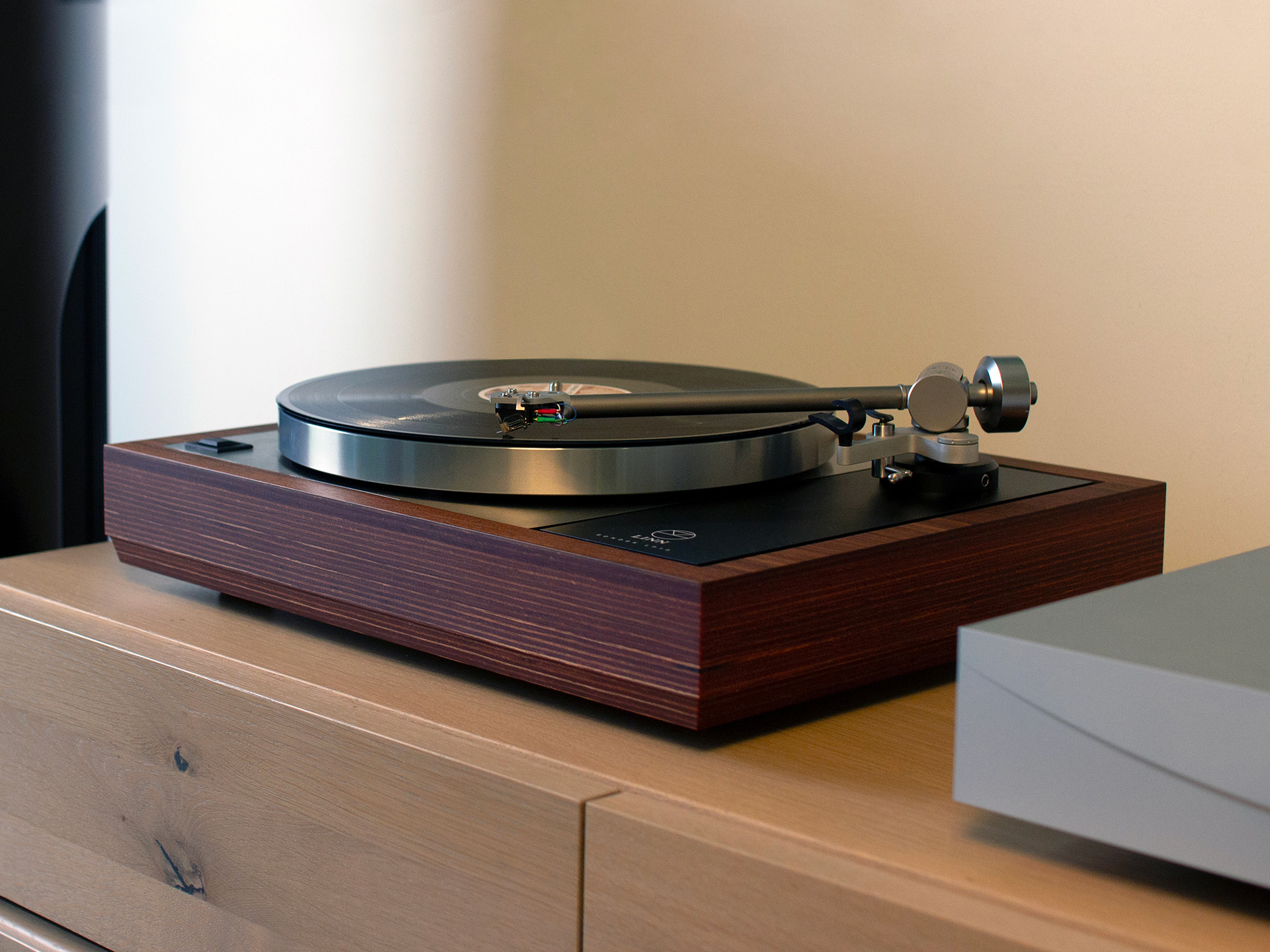 A modern turntable with a wooden base plays a vinyl record, set on a light wood surface. The scene conveys a nostalgic and sophisticated ambiance.