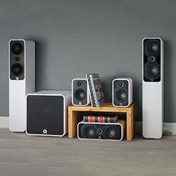 Audio system with two tall speakers, two smaller ones, a subwoofer, and a center speaker on a wooden stand. Books are placed between the small speakers.