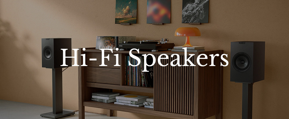 A modern living room features sleek black hi-fi speakers on stands. A wooden cabinet holds records, with a warm lamp above. Art decorates the beige walls.