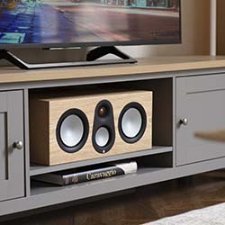 Modern living room setup with a flat-screen TV on a stand. Below, a wooden bookshelf speaker and book are neatly arranged on a gray shelf, creating a cozy ambiance.
