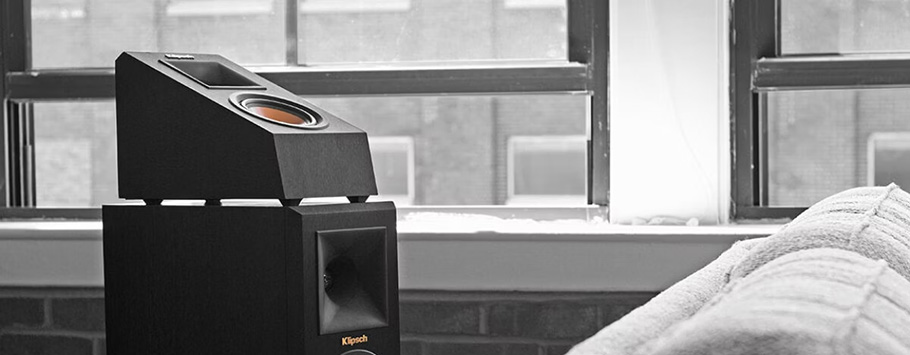 A sleek black speaker with modern design sits in a cozy room near a large window. Natural light highlights the speaker's smooth lines, creating a minimalist and calm ambiance.