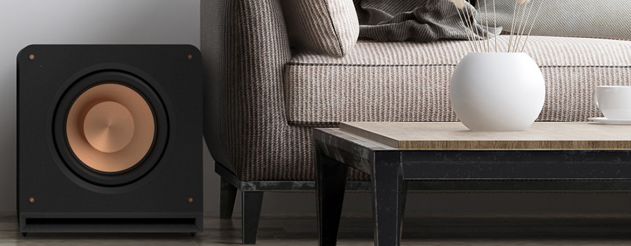 Modern living room with a black subwoofer beside a textured beige sofa. A minimalist wooden coffee table with a white vase and cup adds elegance.