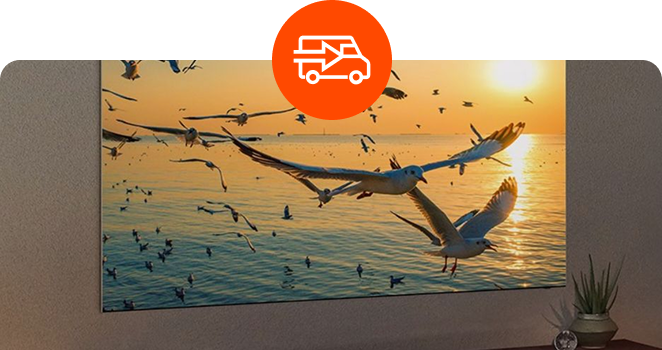 A large television screen mounted on a wall displaying a flock of seagulls flying over the ocean at sunset, with a circular orange delivery truck icon overlaid at the top center.