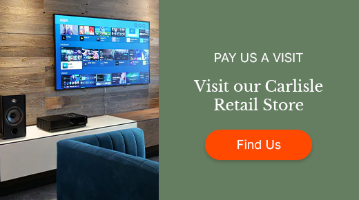 Alt text: "Living room with a TV on a wooden wall, a sound system, and a blue couch. Text invites a visit to the Carlisle Retail Store. Button: 'Find Us.'"
