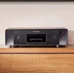 A sleek black stereo receiver with a digital display sits atop a wooden surface. It has knobs on each side, and the surroundings are minimal and modern.
