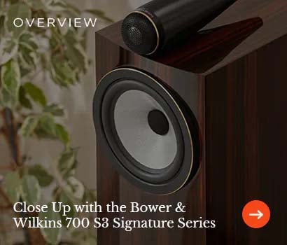 Close-up of a Bower & Wilkins 700 S3 Signature speaker, showing the sleek design and speaker cone. Calm tones, with a plant in the background.