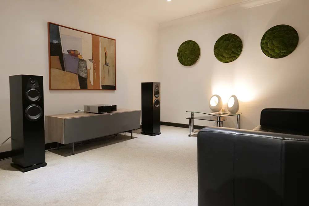 A modern living room with black speakers flanking a wooden media console, abstract art on a cream wall, and round green accents. Soft, ambient lighting.