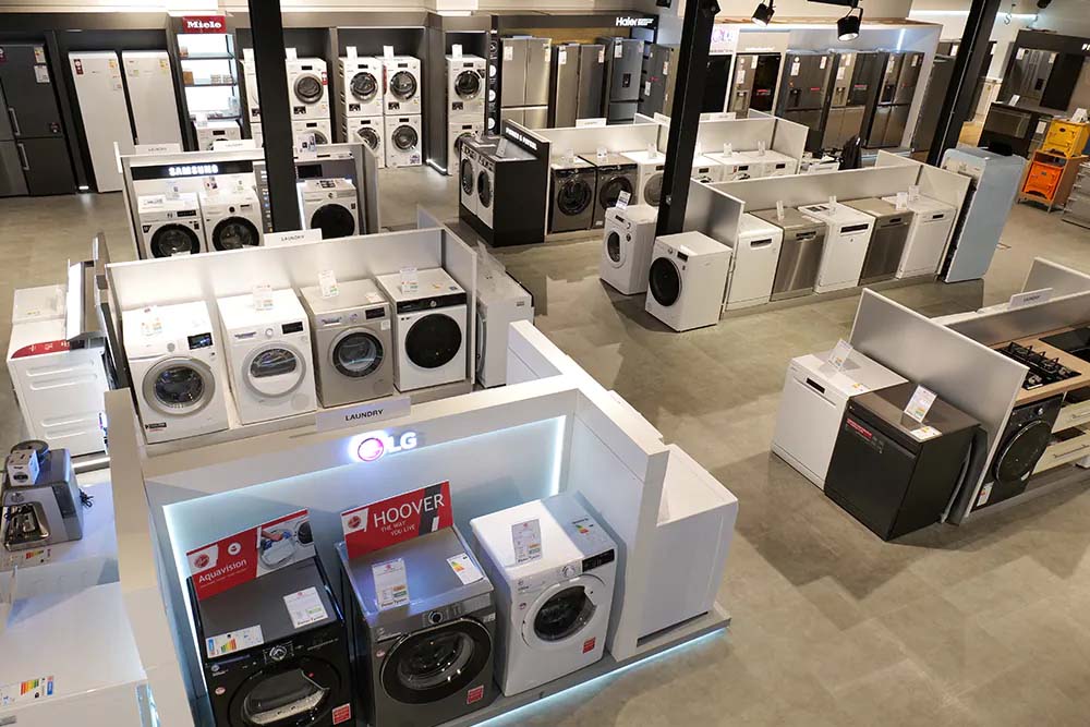 A spacious appliance store showcases neatly arranged washing machines, refrigerators, and ovens. Bright lighting and sleek designs create a modern, organized feel.
