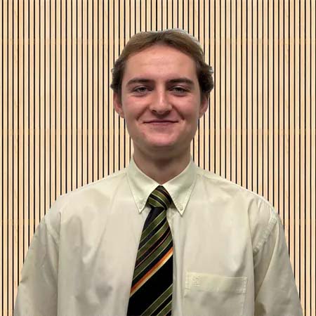 A person wearing a light dress shirt and striped tie stands smiling against a backdrop of vertical beige stripes, conveying a professional and friendly tone.