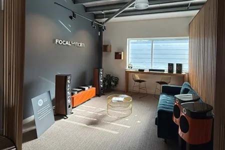 Sunlit room with modern decor, featuring audio equipment and speakers. A teal couch and table sit near a window, creating a cozy, inviting atmosphere.