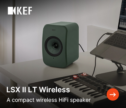KEF promotional banner for the LSX II LT Wireless loudspeaker system featuring the headline "LSX II LT Wireless" and subtext "A compact wireless HiFi speaker". The banner showcases a modern home music studio or desktop production setup. A single sage green compact bookshelf speaker sits on a white desk next to a laptop resting on a stand. In the foreground, a compact MIDI keyboard controller with drum pads is visible. The white KEF logo is located in the top-left corner, and a bright orange circular action button with a white right-pointing arrow sits at the bottom-right corner.