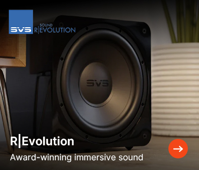 SVS promotional banner highlighting the R|Evolution campaign with the headline "R|Evolution" and subtext "Award-winning immersive sound". The banner features a close-up, front-facing view of a powerful black cube subwoofer resting on the floor in a home interior setting. The subwoofer's large driver prominently displays the SVS logo on its central dust cap. A modern wooden table leg is visible on the left and a white ribbed textured planter sits to the right. The blue square SVS logo alongside the "SOUND R|EVOLUTION" text is positioned at the top left, and an orange circular action button with a white right-pointing arrow is located in the bottom right corner.