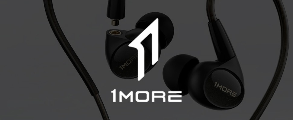 Close-up of black 1MORE in-ear headphones with sleek design on a grey background. The 1MORE logo is visible on the earbuds and to the left.