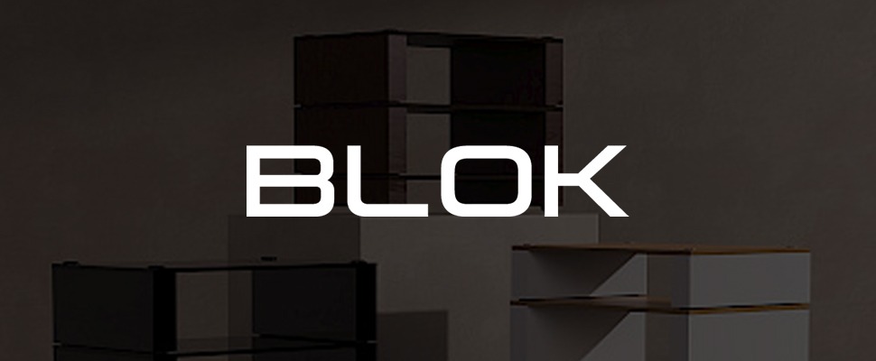 Minimalist room with geometric storage units in black and white on platforms, set against a grey wall. The word "BLOK" is visible.