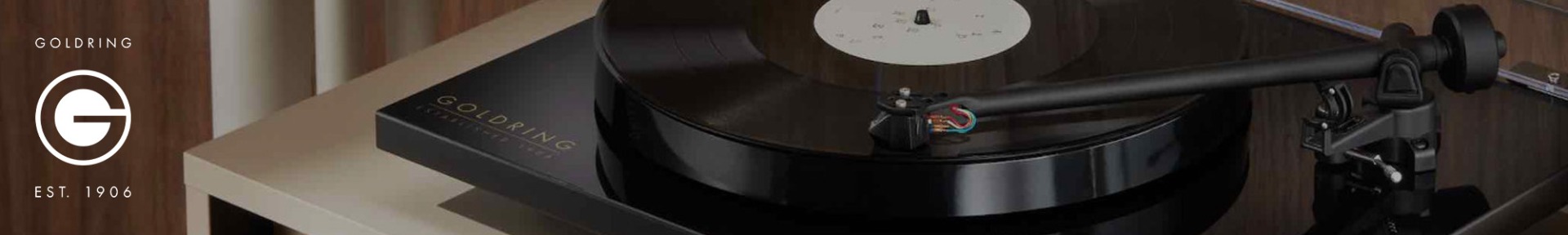 Turntable close-up: A black vinyl record spins on a sleek, modern turntable. The Goldring logo, with "Est. 1906," is visible.