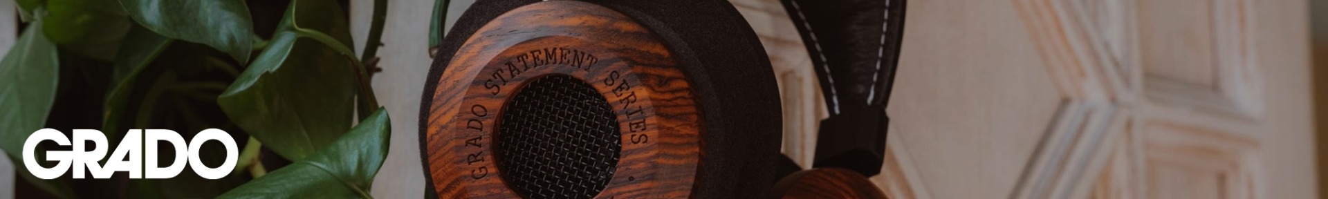 Close-up of a wooden-cased Grado headphone labeled "Statement Series," set against green leaves and a white textured background.