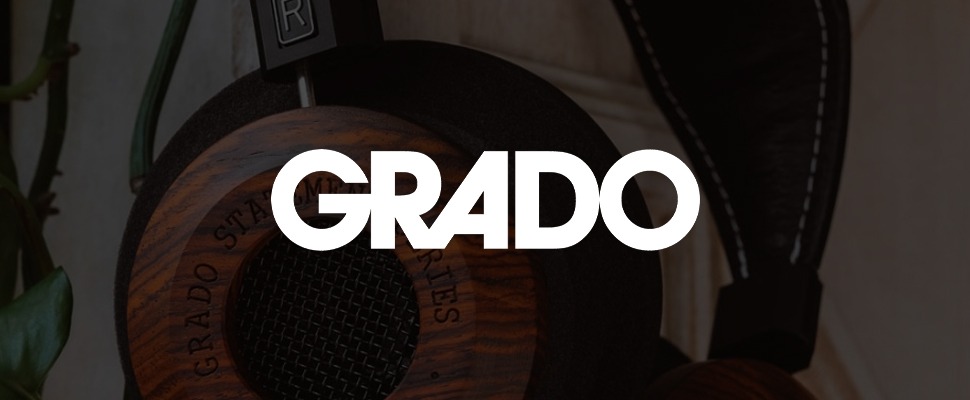 Close-up of a wooden-cased Grado headphone labeled "Statement Series," set against green leaves and a white textured background.