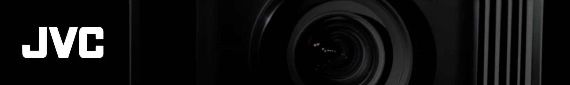 Close-up of a black camera lens on the right against a dark background. The bold white "JVC" logo appears on the left, creating a sleek, professional tone.