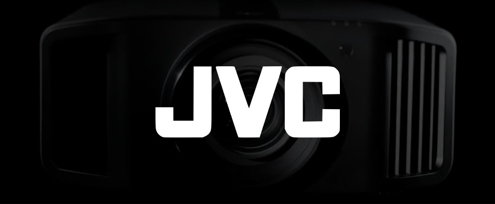 Close-up of a black camera lens on the right against a dark background. The bold white "JVC" logo appears on the left, creating a sleek, professional tone.