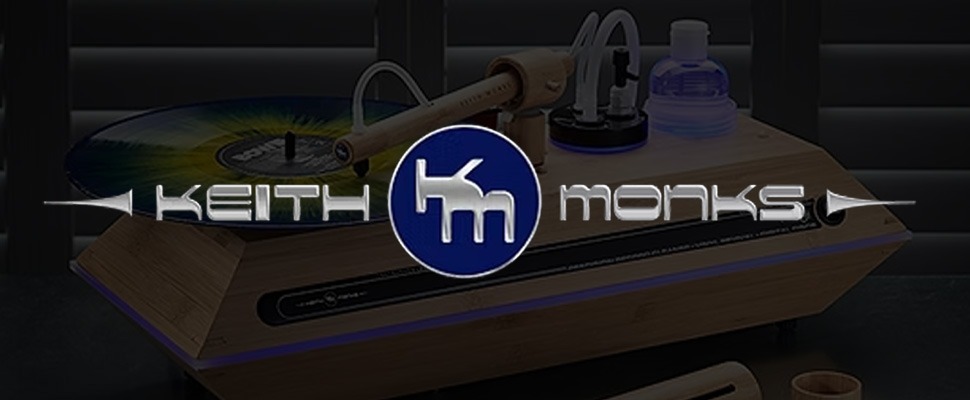 A vinyl record is spinning on a wooden turntable, partially visible with the logo 'Keith Monks' in metallic font overlaying the image.
